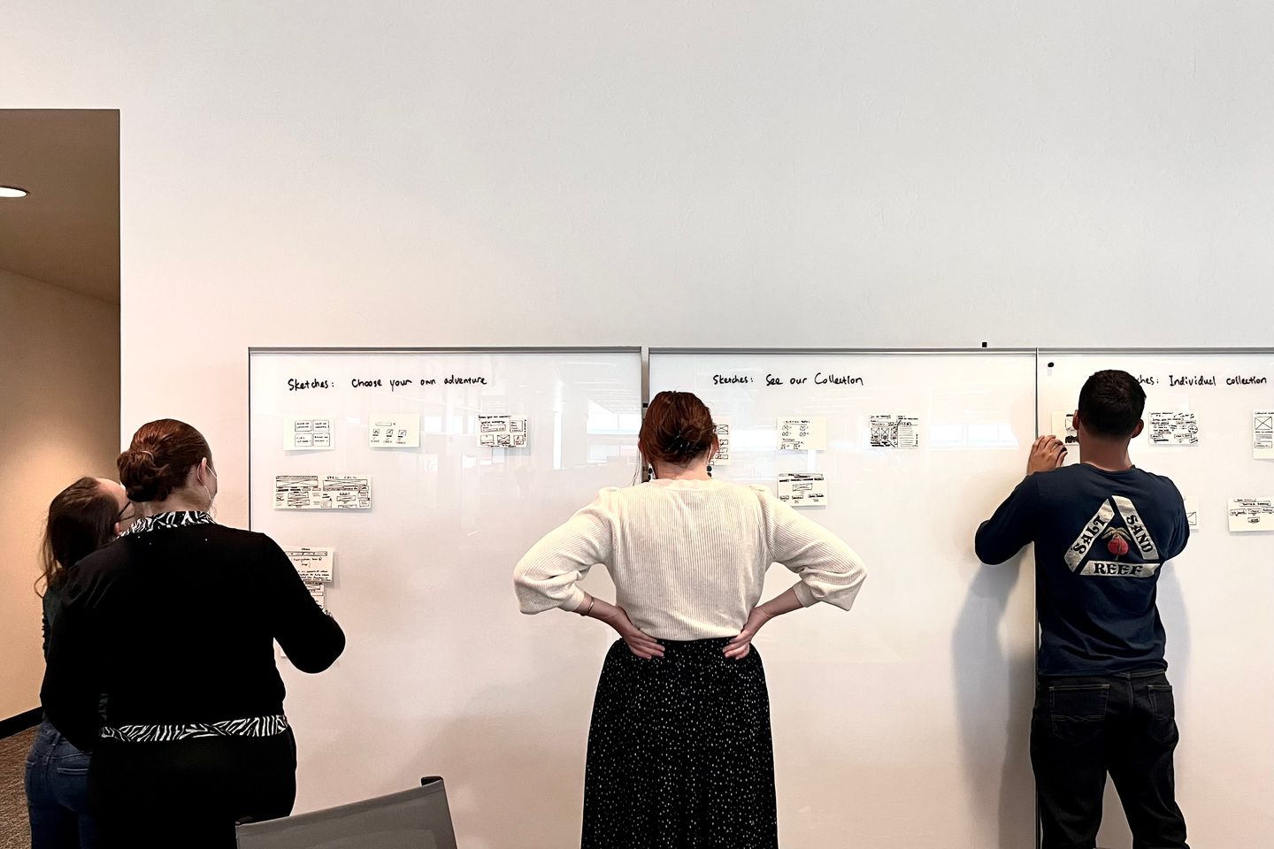 Four people standing in front of whiteboards that have sketches on them