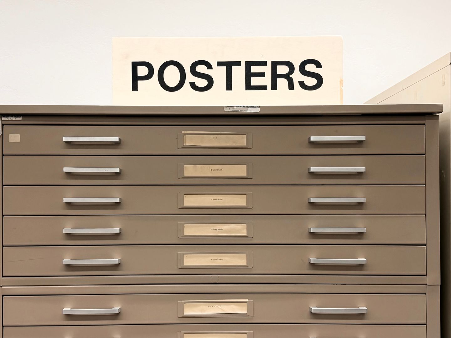 Old signs of different sizes on a chest that says POSTERS in the library space