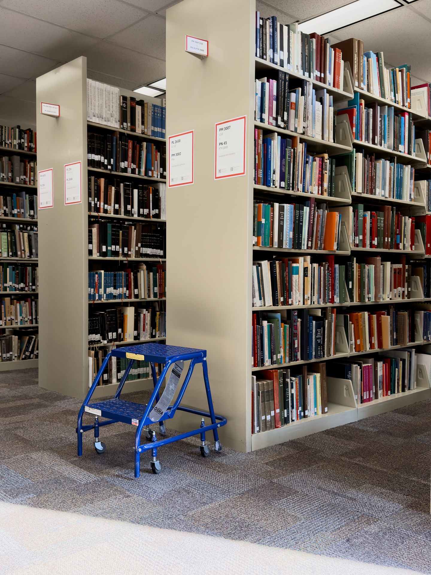 Redesigned signs on library stacks with a stepping stool placed nearby